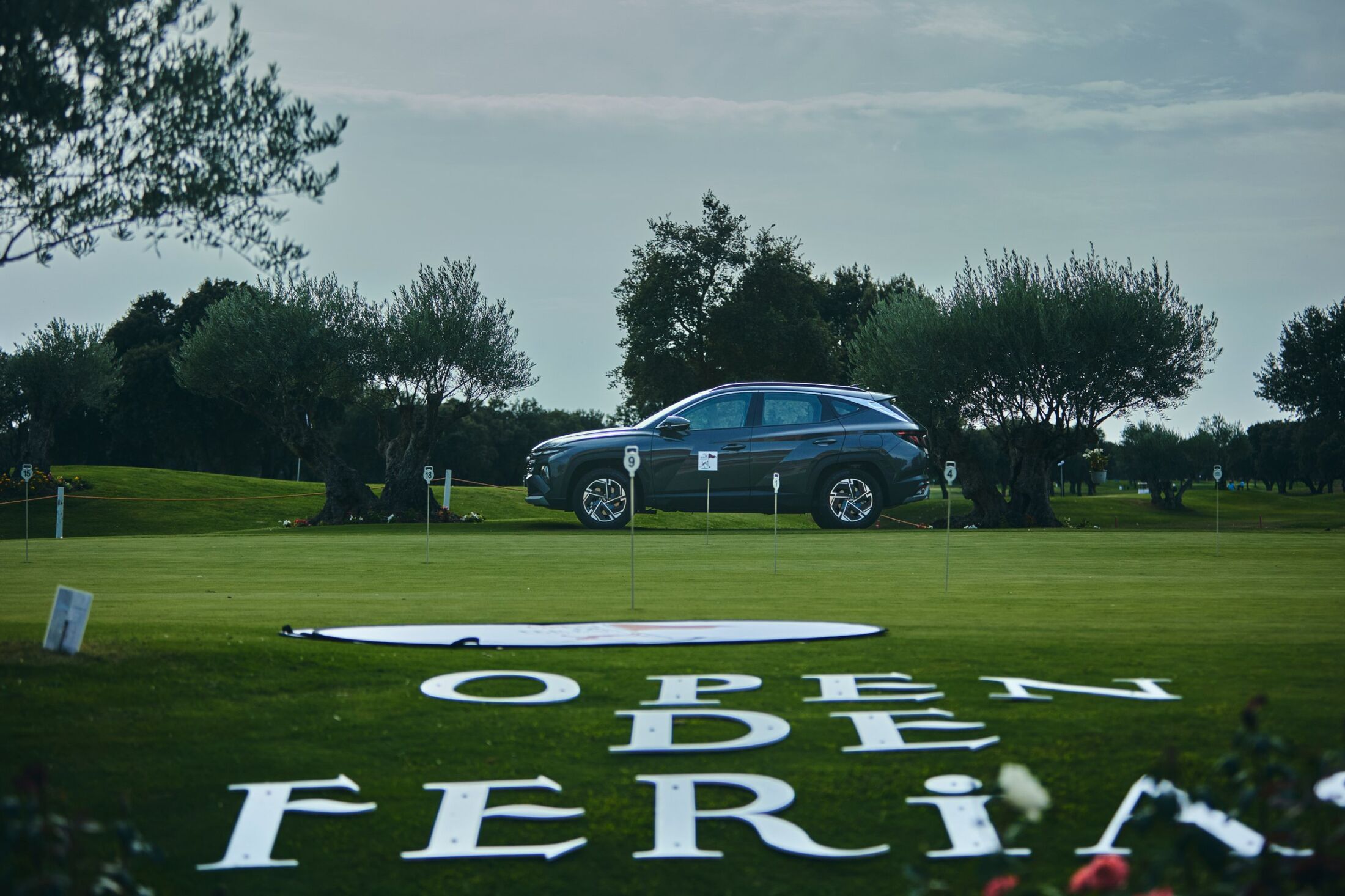 Vehículo de un patrocinador sobre el putting green, con el nombre del Open escrito en el césped